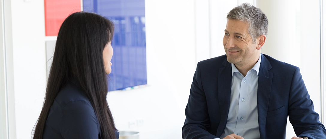 A man and a woman sitting across from each other, engaged in a business discussion.