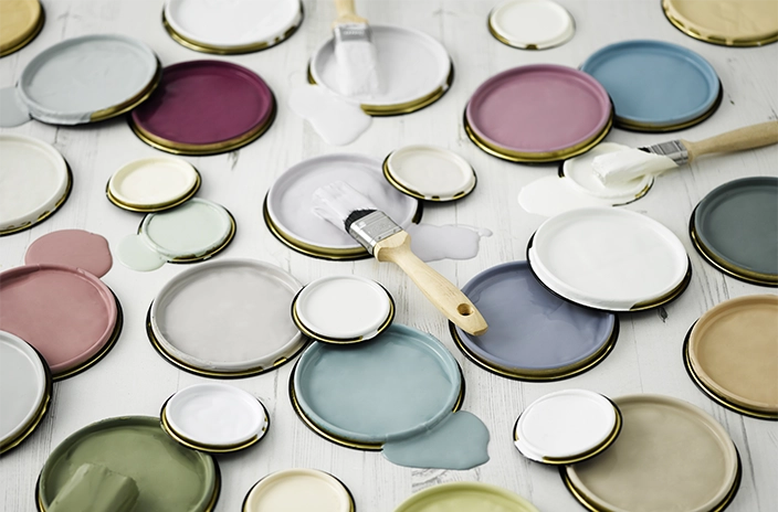 Open paint can lids with different colors of paint and paintbrushes on a white surface.