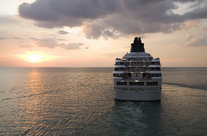 A cruise ship sailing into the distance at sunset, with soft light reflecting on the water.