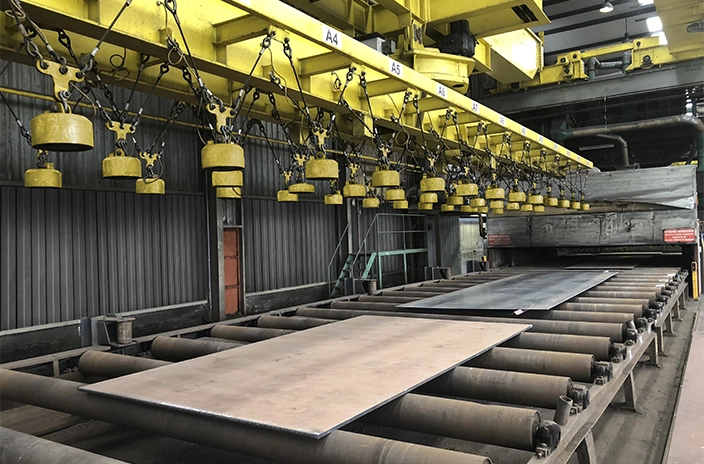 Industrial hall at Brabant Groep with a conveyor belt carrying metal sheets and a crane system with magnets for handling heavy metals.