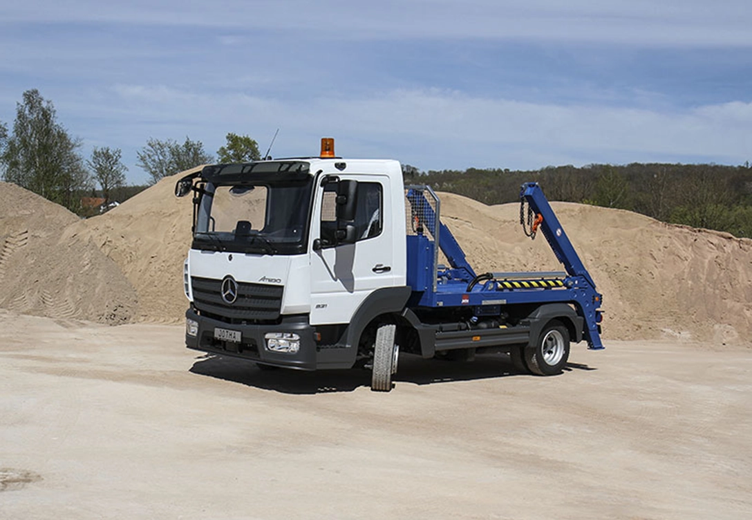 White Jotha Fahrzeugbau truck with a blue hydraulic lift, parked in a sandy area.