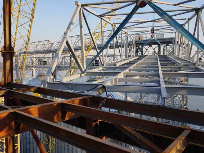 Steel framework under construction, with cranes and scaffolding visible in the background.